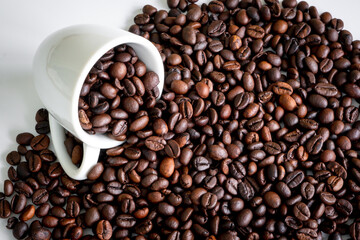 Fototapeta premium Dark roast coffee beans and the white cup background, top view