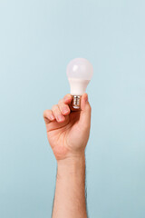 Hand holding a LED light bulb on blue background. Using economical and environmentally friendly light bulb concept. Idea. Energy saving lamp in woman's hand