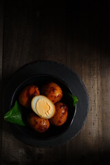boiled eggs cooked in soy sauce in a black bowl in dark background