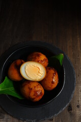 boiled eggs cooked in soy sauce in a black bowl in dark background
