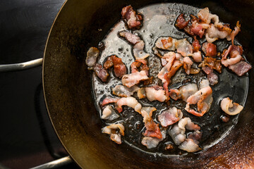 Chopped bacon crispy fried in an iron pan on the black stove, copy space, high angle view from...