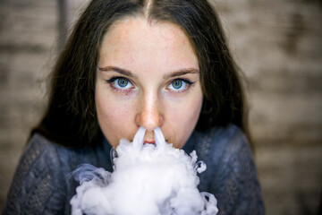 Vaping teenager. Young pretty white caucasian teenage girl with long hair smoking an electronic...