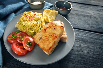 Healthy low carb diet meal with fried tuna steaks, savoy cabbage, tomatoes and lemon on a blue plate and a dark blue rustic wooden table, copy space