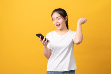 Cheerful beautiful Asian woman holding smartphone on light yellow background.