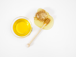 Natural fresh flower honey in bowl and wooden honey dipper on flowing honey drop with bee honeycomb on white background, top view, flat lay