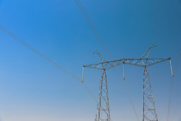 High voltage tower with electricity transmission power lines against blue sky, low angle view