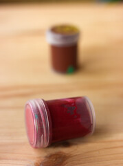Dark red gouache paint on natural beige wooden background. Close-up view