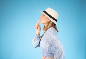 Young woman standing over isolated blue background asking to be quiet with finger on lips. Silence and secret concept.