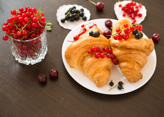 Sweet rolls. Berries. Fresh croissants and ripe red currants, black currants, cherries
