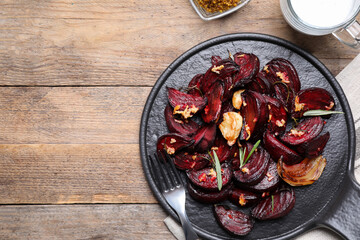 Roasted beetroot slices, garlic and rosemary on wooden table, flat lay. Space for text