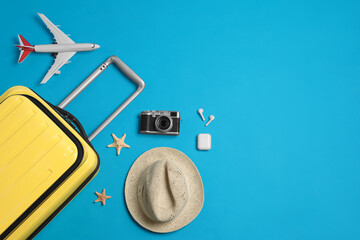 Flat lay composition with suitcase and travel accessories on light blue background, space for text. Summer vacation