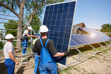 Team of four technicians working on exterior voltaic solar panel system installation in rural...