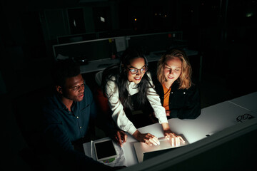 Successful multiethnic business team working on laptop over office desk at night - Powered by Adobe