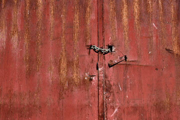 Rusty metal background. Red old and broken metallic door. Closed door with a padlock