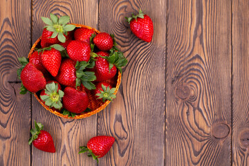 Top view of juicy strawberries in a wicker bowl on a brown shabby rustic wooden table