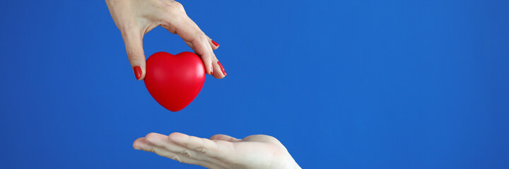 Close-up of person putting red heart on hand on blue background. Motherhood and protection. Copy space in right side. Family relationship and charity and adoption concept