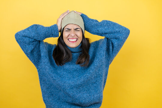 Young beautiful woman wearing blue casual sweater and wool hat suffering from headache desperate and stressed because pain and migraine with her hands on head