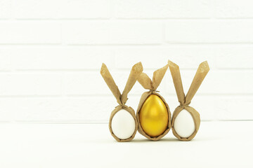 Funny decorated and painted golden eggs stand on a white table in the kitchen. Banner
