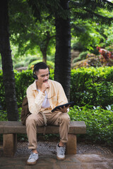 Fototapeta premium A young asian man chilling and relaxing by listen to music with headphone in the park. Good feeling of the sunny day at the garden in the vacation leisure time.