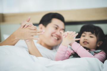 Family time and parenthood leisure concept - father spending time with his little daughters playing hand game symbol and lying on bed at home