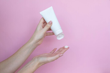 Woman's hands with a tube and a swatch of cream on a pink background. Cosmetic products concept. Copy space