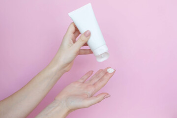 Woman's hands with a tube and a swatch of cream on a pink background. Cosmetic products concept. Copy space