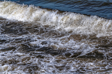 A sea wave creates foam on the water
