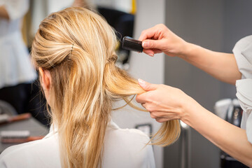 Fototapeta premium Rear View of a hairdresser combs blonde hair of the young woman in a beauty salon