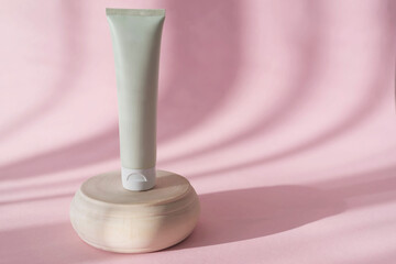 Fototapeta na wymiar cosmetic tube of cream on wooden podium on pink background with sunlight and shadows. Copy space