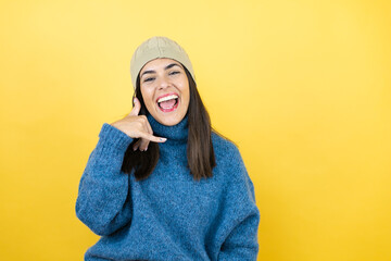 Young beautiful woman wearing blue casual sweater and wool hat smiling doing phone gesture with hand and fingers like talking on the telephone
