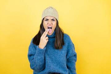 Young beautiful woman wearing blue casual sweater and wool hat disgusted with her hand inside her mouth