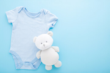 White teddy bear on new baby boy bodysuit on light blue table background. Pastel color. Closeup....