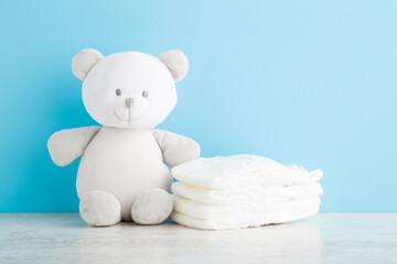 Teddy bear and heap of white soft new baby diapers on wooden table at light blue wall background....