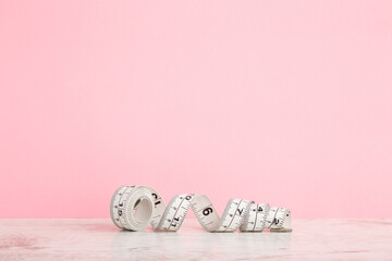 White measure tape on wooden table at light pink table background. Pastel color. Closeup. Front view. Empty place for text.