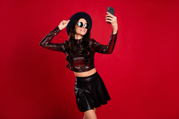 Photo of lady hold phone shoot selfie wear glossy top hat leather short skirt specs isolated red color background