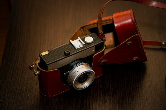 camera in an old leather case, old camera on a wooden table, photographic equipment, retro camera on a brown background, vintage camera, leather case, brown antique