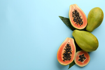 Fresh ripe papaya fruits with green leaves on light blue background, flat lay. Space for text - obrazy, fototapety, plakaty