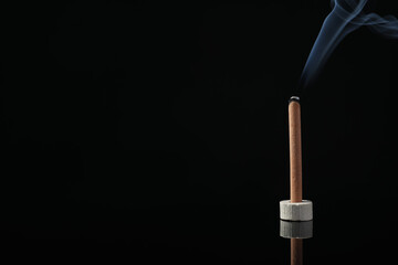 Incense stick smoldering in holder on black background. Space for text