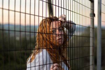 red-haired woman 50 years old in white T-shirt with a very sensitive and relaxing face behind a fence.