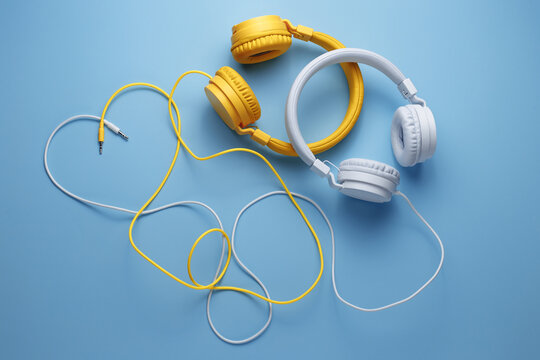 Cute image of two headphones whit cables in heart shape over blue background. Music concept.