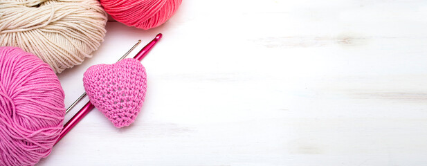 Cute pink heart knitted by hand with threads and crochet hooks on a white wooden background with copy space. Valentine's day background.