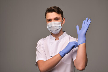 Young doctor wearing blue gloves on gray background