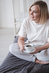 Beautiful young woman drinking coffee on bed on a dark blanket, simple, home, space in the frame.