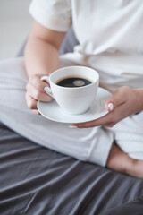 Young beautiful woman having breakfast in bed with coffee in cozy bedroom. Morning rituals. Close-up.