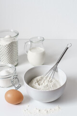 Fototapeta na wymiar Mehl in einer Schüssel, ein Ei und Backzutaten auf einem weißen Küchentisch. Vorbereitung, Teig, Frühstück.