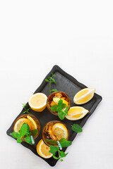Iced tea with lemon slices, mint and ice on white wooden table, top view.