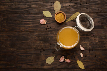 Traditional homemade beef bone broth with vegetable in glass jar on dark rustic wooden background.