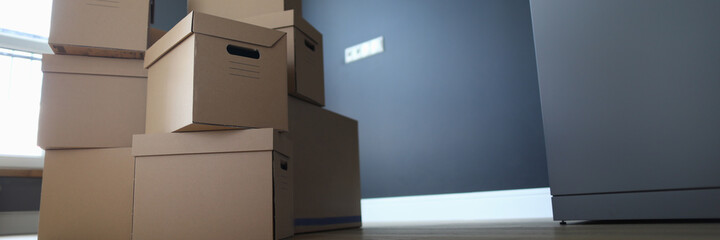 Close-up of unpacked stack of cardboard boxes. Room with personal stuff packed in carton. Purchased apartment or house property. Moving day and renovation concept