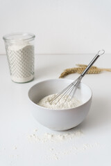 Fototapeta na wymiar Mehl und ein Schneebesen in einer Schüssel auf einem weißen Küchentisch. Vorbereitung, backen, Frühstück.