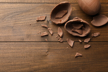Broken and whole chocolate eggs on wooden table, flat lay. Space for text
